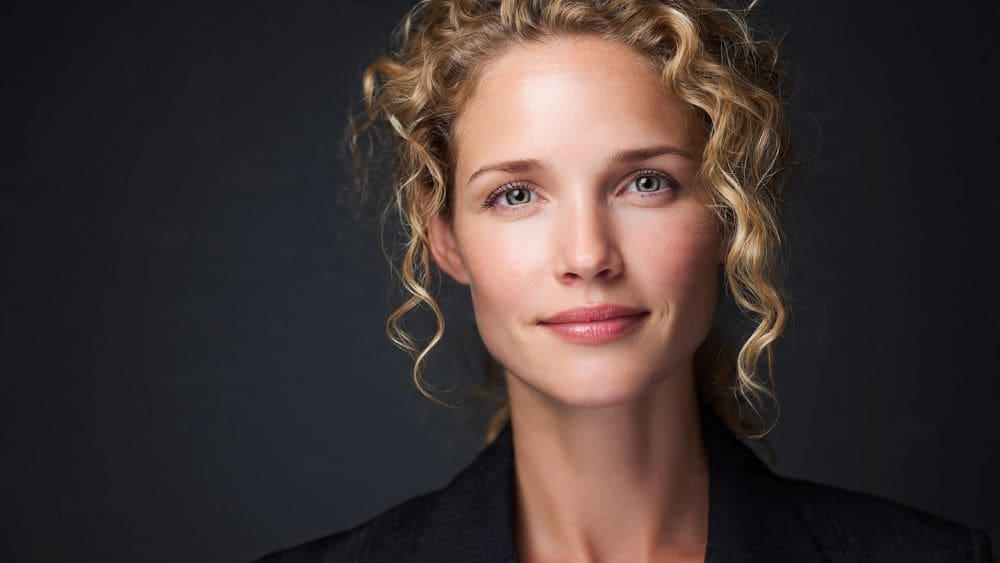 Hyper-detailed 8k portrait of a female executive with soft, glowing skin texture and professional makeup. The lighting is warm and perfectly balanced, creating a polished, magazine-cover aesthetic.