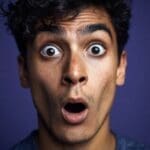 Close-up of a man with curly hair and an extremely shocked facial expression